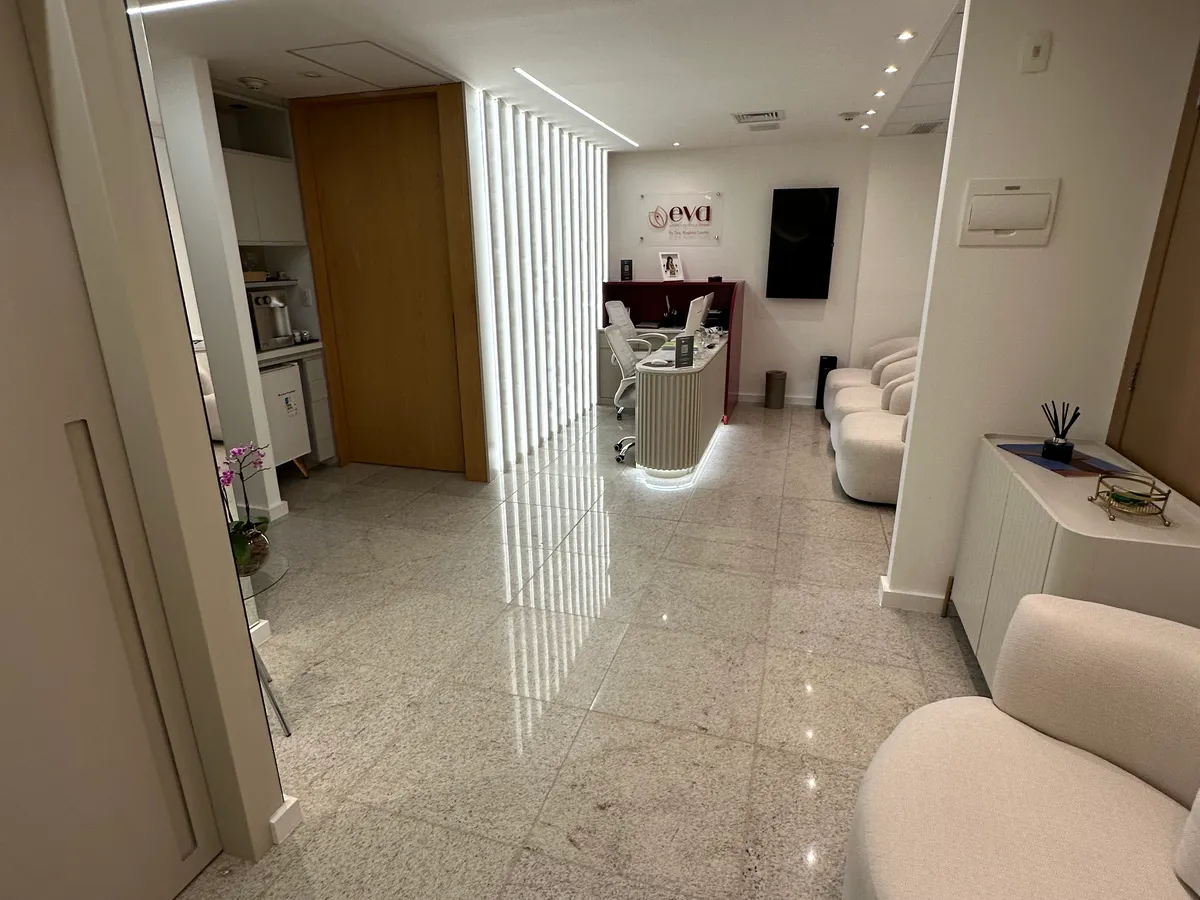 Corredor de entrada e circulação da clínica Eva com iluminação linear e recepção ao fundo