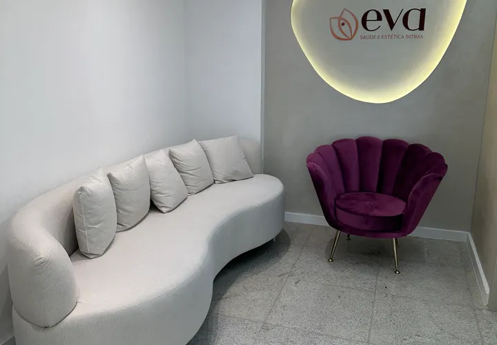 Sala de espera da clínica Eva com sofá curvo, poltrona de veludo e logotipo iluminado na parede